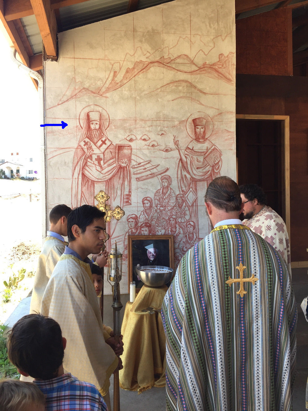 Two priests in liturgical vestments standing in front of a large fresco sinopia for iconography cycle at St Innocent Orphanage.